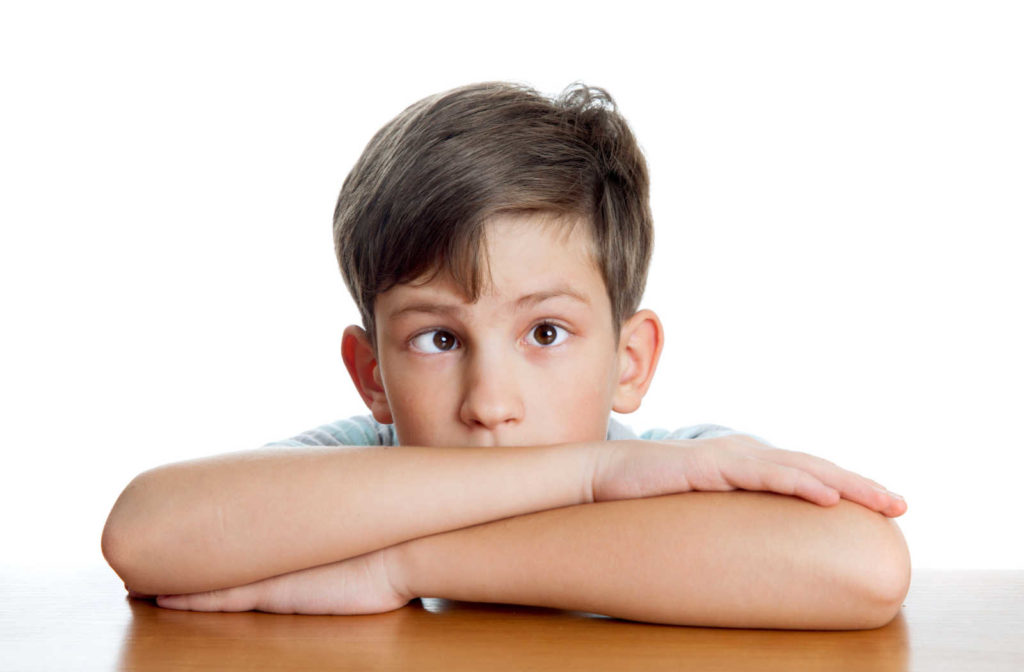 A small boy with strabismus sitting at a table with folding arms and his chin resting on his arms.