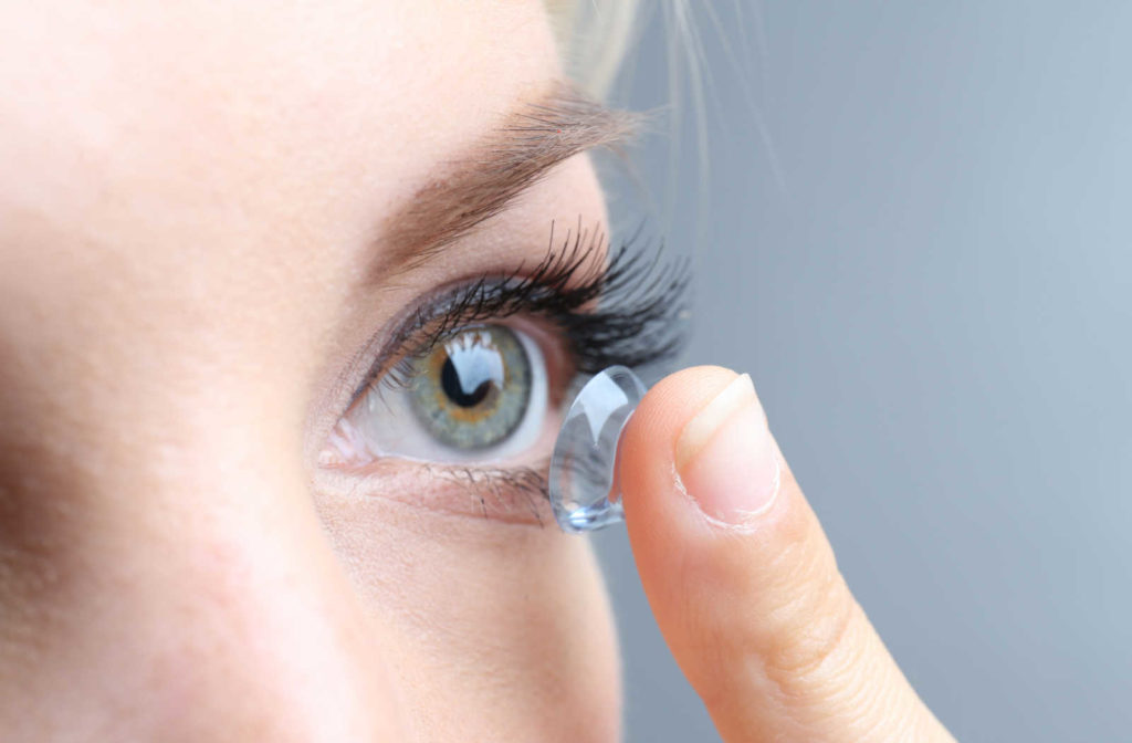 Young woman holding a contact lens close to her eye.