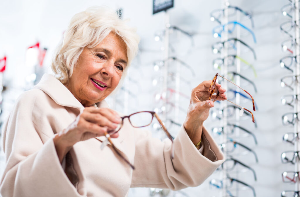 A senior woman trying to choose from the two pairs of glasses she's holding in each hand.