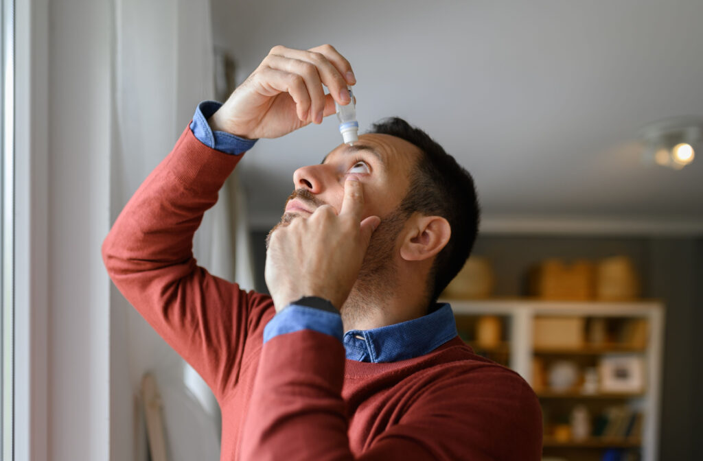 A man looking up, holding his left eye open with his left hand and applying eye drops with his right hand.