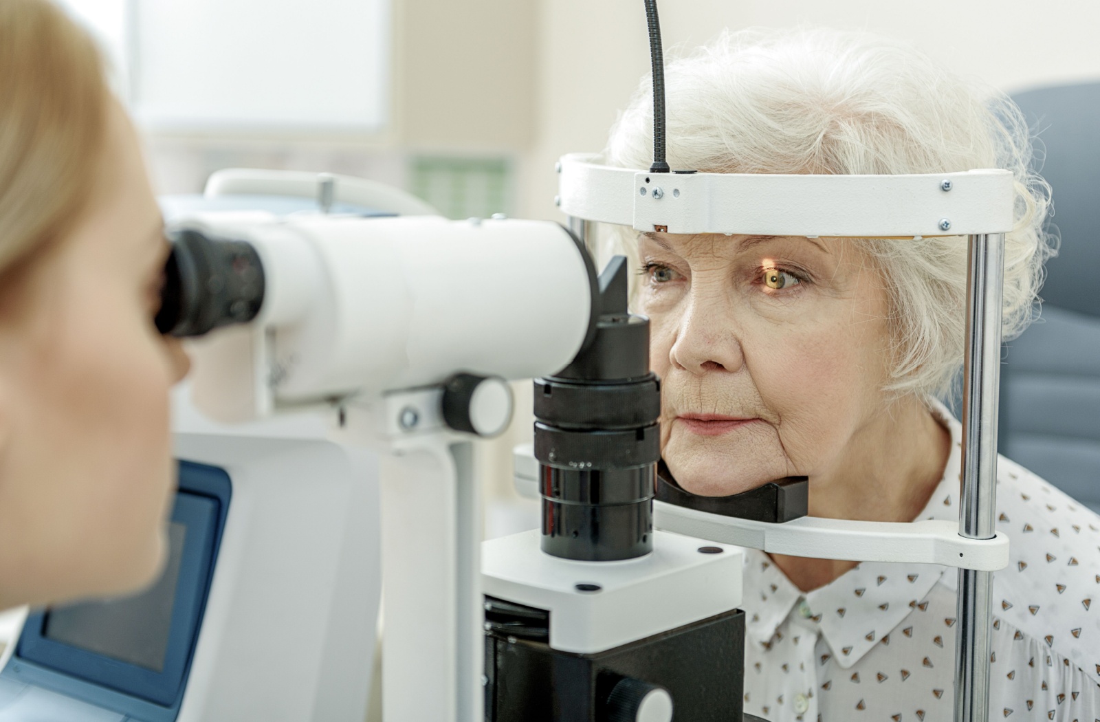An optometrist performing a slit-lamp exam on an older adult woman
